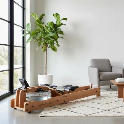 A WaterRower Natural wooden water rowing machine in an elegant living room, crafted from light oak wood, with sunlight streaming through a window.